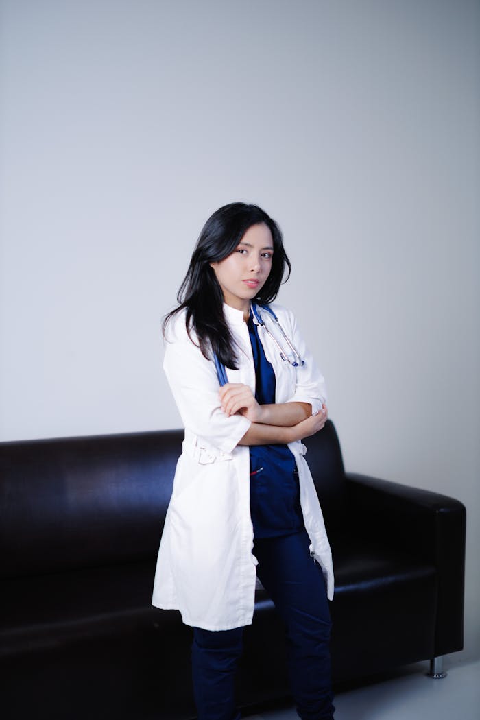 about-us-02 Portrait of a confident female doctor standing in a clinical setting, arms crossed.